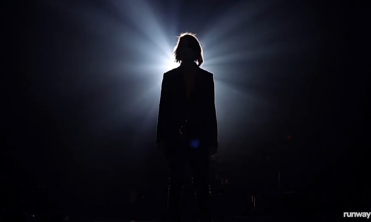 A woman singing and standing in a concert stage with a brigh
